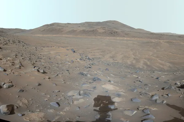 Perseverance rover view of Neretva Vallis in Jezero Crater: dusty reddish ground scattered with dark rocks under a pale sky